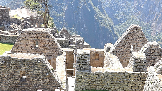 Female tourist sitting on a rock at Machu Picchu and admiring the beautiful view and wearing a facemask - travel destinations concepts