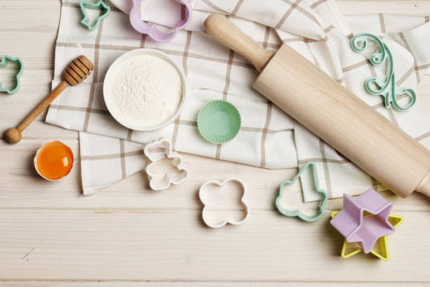 istock Baking utensils and ingredients. Colorful silicone cooking utensils, rolling pin, cookie mold, cupcake cases and sugar sprinkling on a white wooden background. Easter concept. 1844941489