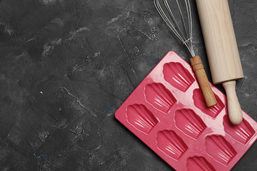 Colorful silicone cooking utensils, whisk, rolling pin on a dark background