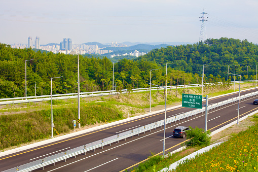 A bustling four-lane road in Ulsan, bordered by lush forests with an onramp to the side, showcasing the city's seamless integration with nature.