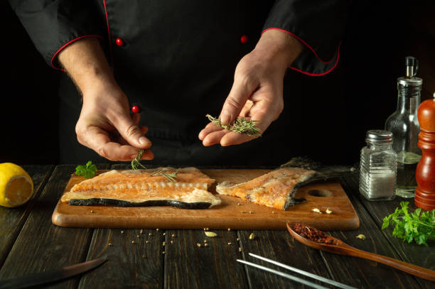 istock We prepare fresh fish on a kitchen cutting board before salting it with aromatic spices. Chef's hand adding rosemary to fish steak 1844974131
