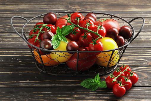 Composition of fresh ripe tomatoes of different varieties, spices, basil, rosemary, thyme, hot pepper in a basket on a wooden board close-up