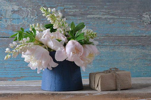 Bouquet of white peonies and lupines in blue jug and hand made gift box on the old blue paint wooden background;