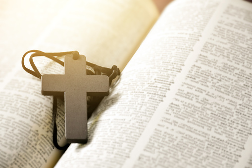 Open Bible holy book and wooden cross beads on a brown wooden table, christianity religion concept.