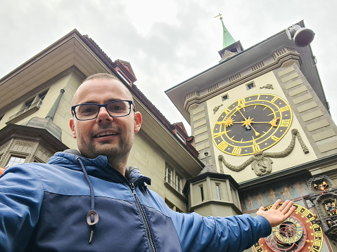 Male tourist taking selfies with his phone in front of the Zytglogge (Clock Tower) in Bern, Switzerland.
