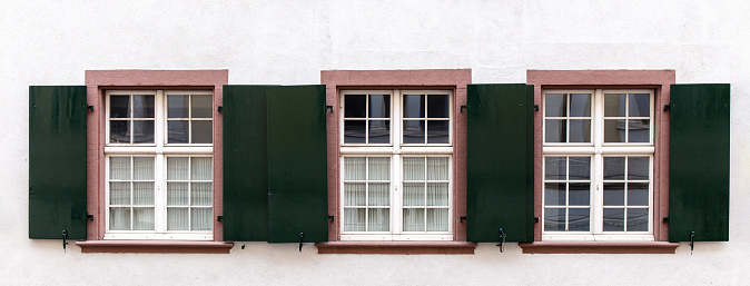 Three windows in a row with dark metal shutters on white wall
