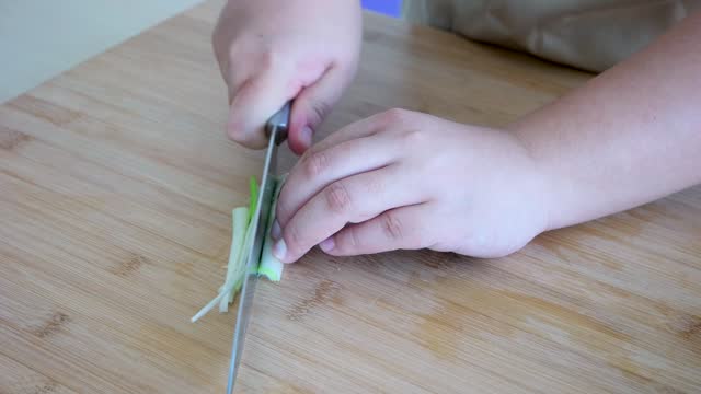 Close up shot of chef's hands using a knife cutting a green onion or spring onion on wooden board.