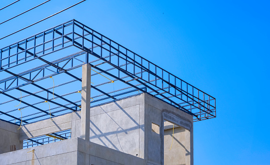 Incomplete precast bare concrete room wall with electric conduit wiring system on roof beam outline on top of modern office building structure in construction site against blue sky background