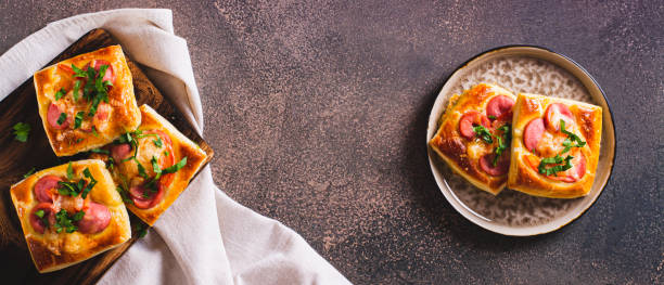 istock Square mini pie baked with tomato, sausage and cheese on a plate for a snack top view web banner 1845058336