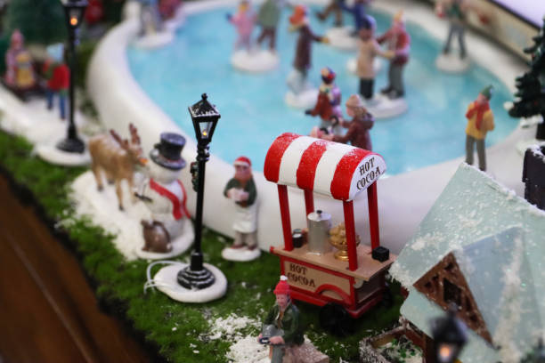 Stock photo showing a beautiful Christmas village display, which features numerous illuminated houses. The houses have been placed on artificial grass and sprinkled with fake snow to create a snowy scene,on top of a chest of drawers, complete with a forest of plastic spruce trees.