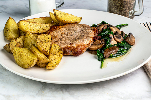 bone less pork chop served with sauteed spinach and  mushrooms with potatoe wedges