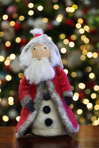Stock photo showing close-up view of homemade needle felt, Santa model in a domestic room decorated for Christmas.