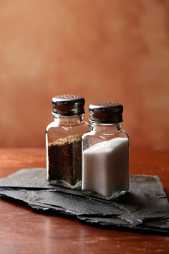 Traditional glass salt cellar and spilled salt on a wood background