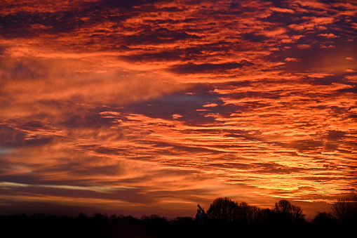 A dramatic dawn deep orange and red sky with the sun rising behind the tree line, horizon