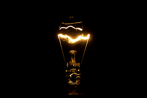 Close up of a vintage light bulb with glowing filament isolated on black background