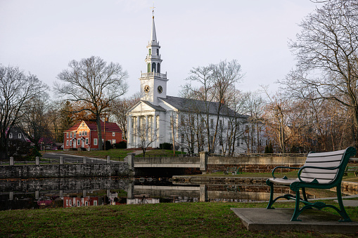 Milford Cityscape in winter over the Wepawaug River with views of the First Church of Christ in Milford built in 1824, stone bridge, and bench at the Lower Lagoon Park green in Connecticut