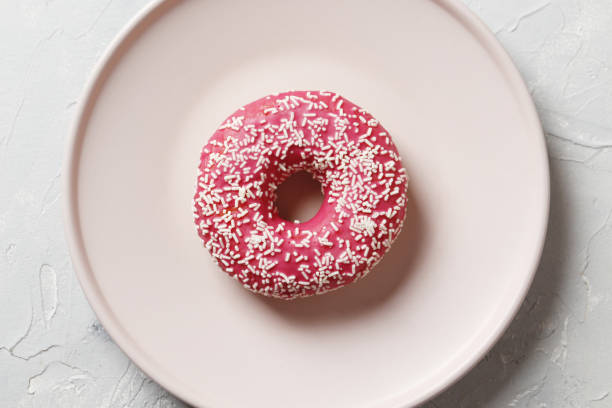 istock Delicious colorful donuts with sprinkles on stylish plate on white table with confetti, flat lay. Party concept. No diet. Candy bar at wedding reception. Purple and pink donuts 1845268953