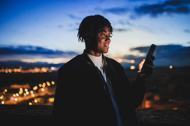 Young adult with a smartphone during a dusk, with the blurry city lights visible behind them. stock photo