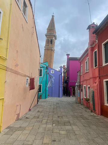 Burano, Italy - November 3 2023: Calle Tibaldon street with a view to the tilting bell tower of the Church of San Martino.