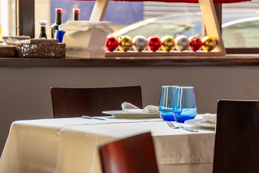 Empty table in a restaurant, with white tablecloth and blue glasses