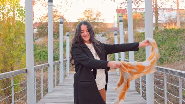 Woman in a coat moves and plays with a scarf at sunset