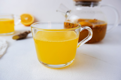 Sea buckthorn tea with orange and ginger in glass cups on a light background. Herbal vitamin tea