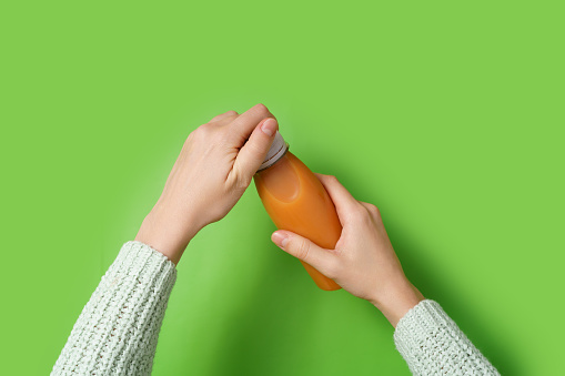 Woman holding orange juice in a plastic bottle on green background