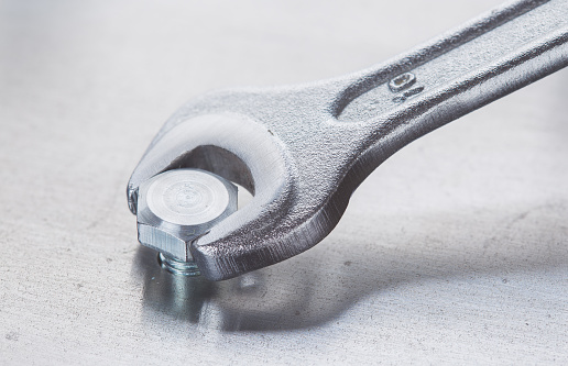 Wrench tightens bolt in steel billet. Spanner, bolt, screw and nuts.