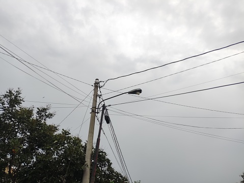 Utility and electricity cables hanging on poles in hill area with cloudy clouds.