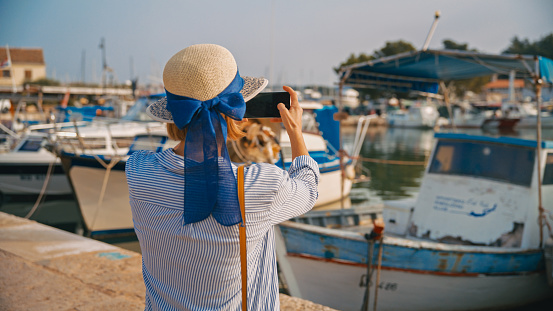 In the picturesque town of Novigrad,Croatia,a rear view reveals a female tourist capturing the essence of the harbor through her smart phone. A moment of modern exploration seamlessly woven into the historical tapestry of coastal beauty
