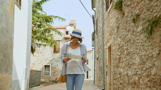 In the charming streets of Novigrad,Croatia,a mid adult woman strolls alongside historic buildings,engrossed in reading a road map. A scene that intertwines historic exploration