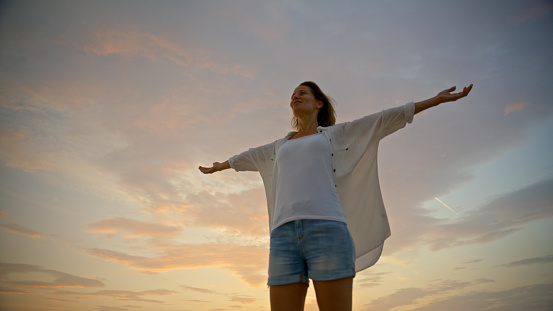 Against the backdrop of a cloudy sky during sunset in Istria,Croatia,a low angle view captures a female tourist standing with arms outstretched. The scene epitomizes a moment of awe and connection with the atmospheric beauty