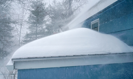 strong wind blowing snow off the roof in blizzard