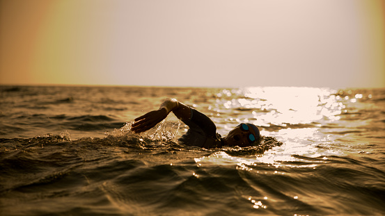 In the determined silhouette of a woman,she swims in the seascape with sunlight reflections against the clear sky during the mesmerizing sunset in Istria,Croatia