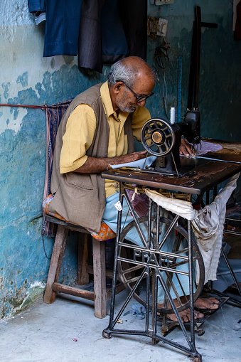 Devprayag, India - Oct 13, 2014 : Street tailor working in his shop on a foot sewing machine in Devprayag, India