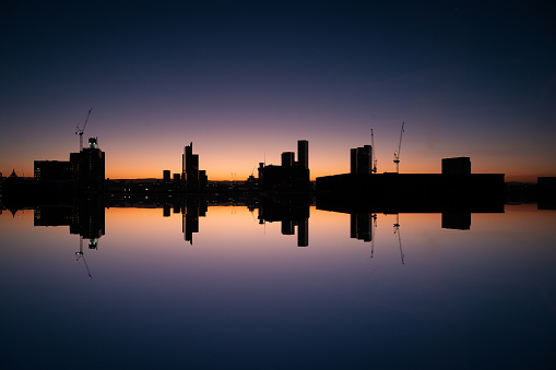 An atmospheric image of Reflection of Manchester Skyline at Sunrise with Skyscraper Silhouettes on the Golden Horizon and Blue Morning Sky