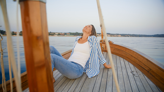 Relishing the tranquility of a summer vacation,a relaxed mid adult woman sits with her head back on the sailboat's bow,surrounded by the sea and sky in Istria,Croatia