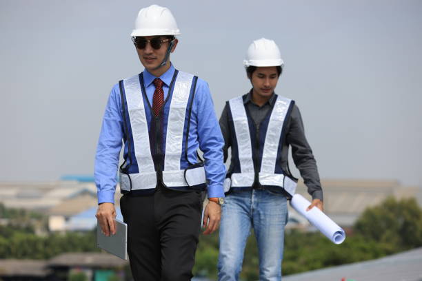 deux hommes ingénieurs portant des gilets de sécurité discutent sur le chantier de construction du toit solaire - 24424 photos et images de collection