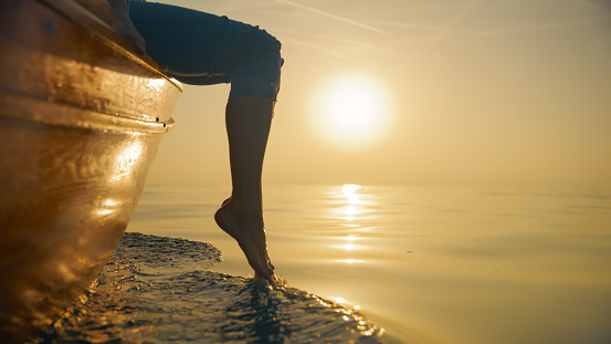 In the enchanting glow of a majestic sunset in Istria,Croatia,a side view and low section capture a woman dipping her legs into the sea water from a boat. The scene adds a touch of tranquility and elegance to the coastal evening ambiance