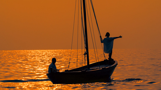 In the enchanting sunset of Istria,Croatia,a rear view captures a woman standing with her arm outstretched on the edge of a sailboat,accompanied by a man on the sea. The scene embodies a shared moment of serenity and connection,as the sun paints the sky in idyllic hues over the Adriatic coast