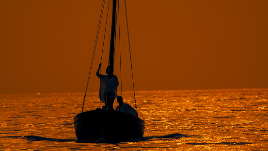 Romantic silhouette of a couple finding serenity,relaxing on a sailboat amidst a vast rippled seascape,under the majestic hues of a sunset in Istria,Croatia. This enchanting scene embodies the romantic allure of the Adriatic coastline