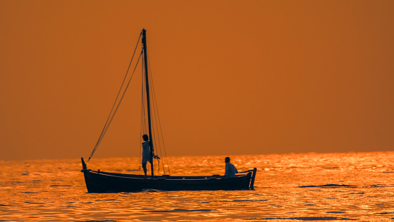 Side view elegance,A silhouette couple peacefully relaxes on a sailboat,sailing through a vast rippled seascape during a majestic sunset in Istria,Croatia. This enchanting scene captures the tranquility and romantic allure of the moment