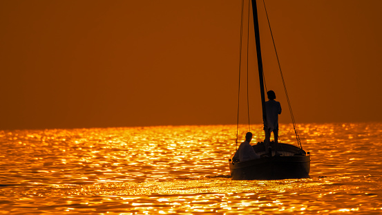 In the picturesque sunset of Istria,Croatia,a rear view of a silhouette couple relaxing on a sailboat in the seascape,with idyllic sunset reflections against the clear sky
