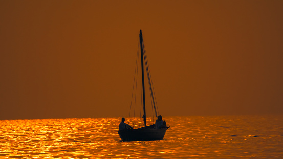 An unrecognizable couple finds tranquility on a silhouette sailboat in the serene waters during an idyllic sunset in Istria,Croatia. The scene captures the essence of shared moments,blending with the enchanting beauty of the Adriatic as the sun gracefully sets on the horizon