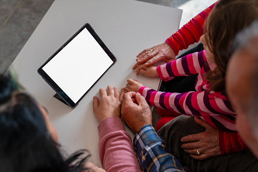 High angle photo of multi generation family members' hand next to digital tablet. They are looking at the digital tablet screen. The screen is blank. Shot under daylight.