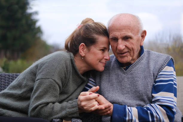 Elderly father and daughter holding hands Elderly father and daughter sitting side by side in the garden and lovingly holding hands.The woman smiles at her father with her hand resting on his. A photo of a family visiting and lovingly caring for their father. father daughter 80s stock pictures, royalty-free photos & images