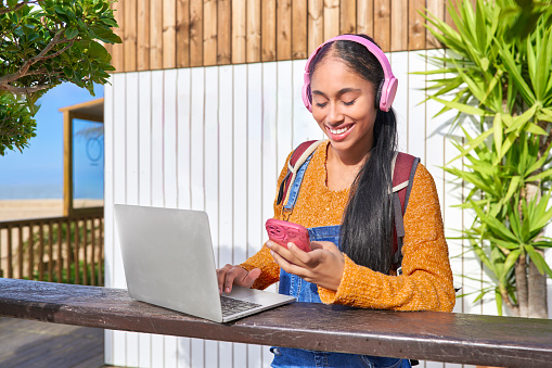The digital nomad Colombian girl listens to music with her headphones and her smart phone while reviewing the sales of her e-commerce business