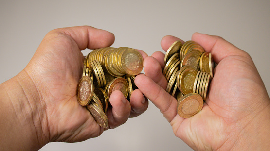 Two hands holding many coins of gold color with silver.