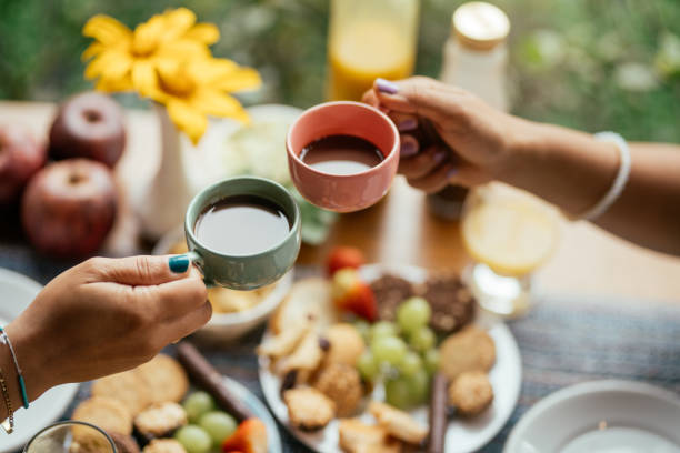 Couple drinking coffee together over breakfast on the patio of a BnB Close-up of a young couple toasting with cups of coffee while having breakfast outside on the patio of a BnB gay dinner table stock pictures, royalty-free photos & images
