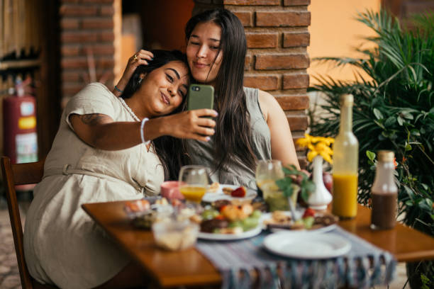 Young couple taking selfies during breakfast on the patio of a BnB Affectionate young lesbian couple taking a selfie during breakfast together on the patio of their accommodation in the morning gay dinner table stock pictures, royalty-free photos & images